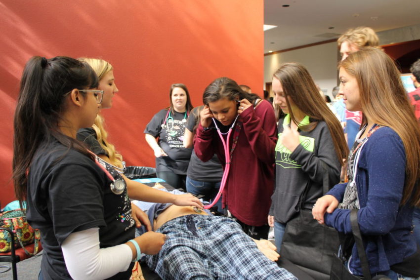 Nursing students offer visiting high school students the opportunity to listen to sounds within the body using a simulation manikin.