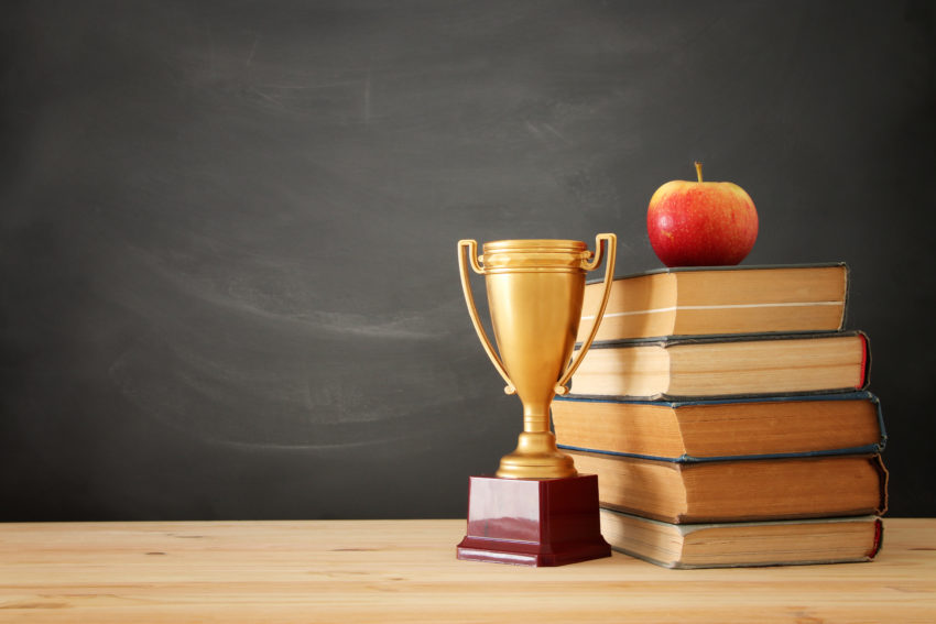 Trophy in front of stack of books with apple on top.
