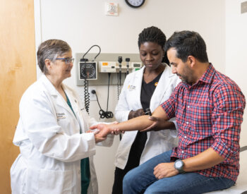 A physicians assistant professor and student performing a test on a latino male.