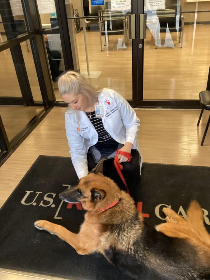 Dr. Meredith Stensland sits at the entrance of a dialysis clinic with Buddy, a German shepherd therapy dog.