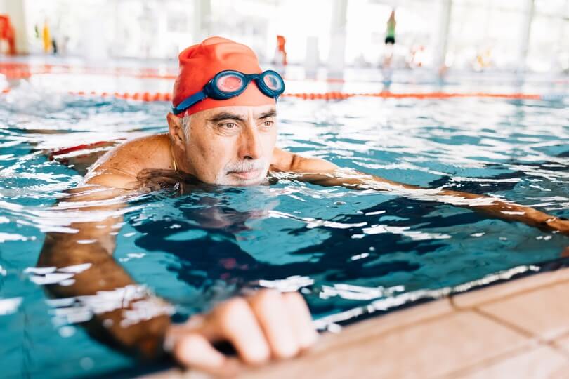 Photo of older man in a pool with a swimmer's cap and goggles