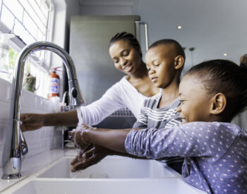 Woman and two children, a boy and girl, washing their hands at a white double sink.