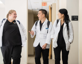 Physician assistant studies students talk as they walk down a hallway.
