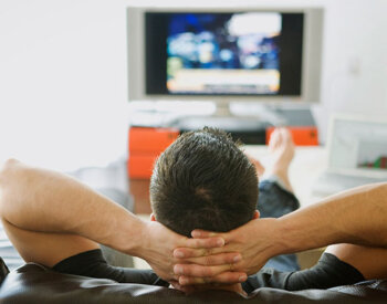 Back of man's head with hand interlocked watching a TV. 