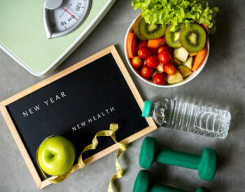 Fresh vegetable salad, sport equipment and scale grouped together with black board reading New Year, New Health.