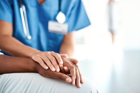Focused photo of a health provider and a patient clasping hands.