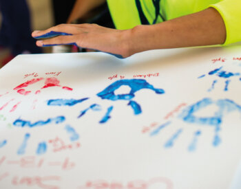 A child prepares to press their painted alongside other handprints.