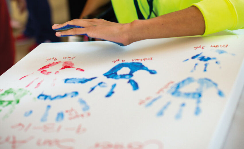 A child prepares to press their painted alongside other handprints.