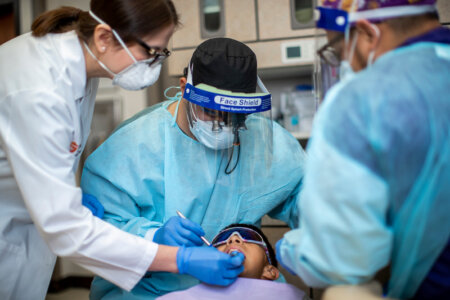 A dental faculty member leans over the shoulder of a dental resident to offer guidance during a procedure.