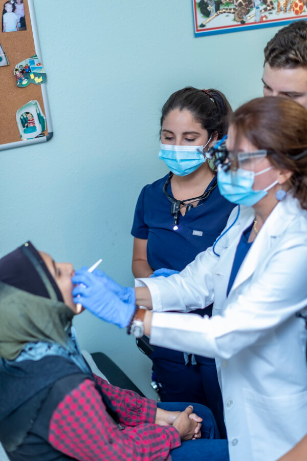 Dr. Farokhi wears her dental loupes to examine a patient while students observe at her side.