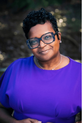 Dr. Fayron Epps smiles wearing a purple top and black-rimmed glasses.