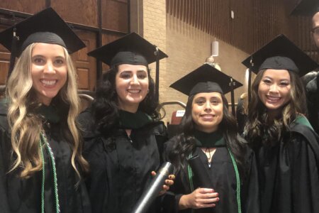 Four physician assistant graduates stand side-by-side in their regalia.
