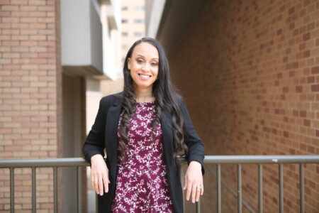 Shanae Rhodes rests her elbows on the railing behind her while smiling.
