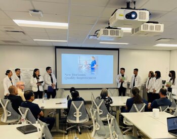 Nursing students presenting their findings to a room full of nursing education leadership.
