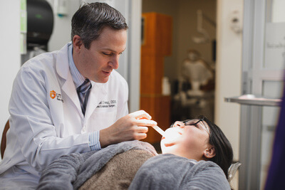 Dr. Perez examines a patient's mouth while she is reclined in the dental chair.