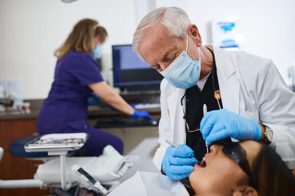 A dentist performs an oral examination on a patient in the dental chair.