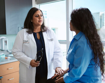 Sukeshi Patel Arora, MD, speaks with a woman in blue shirt in a clinical space.
