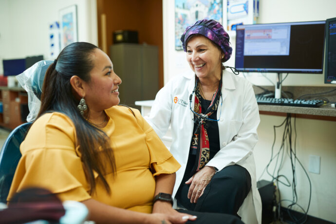 A female dentists smiles with her female patient who is sitting in a dental chair.