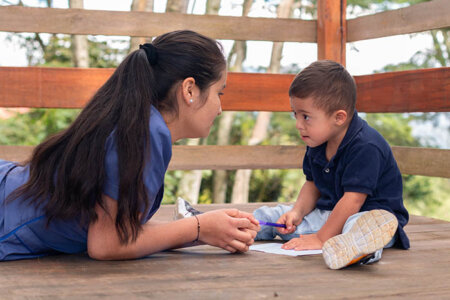 Woman in blue uniform teaching writing to a child with Down syndrome.