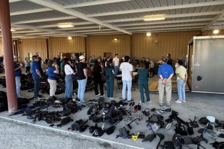 Volunteers listen to a speaker surrounded by wheelchair seats and wheels.