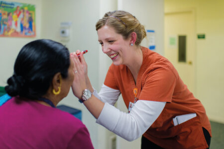 A nursing student shines a pen light into a patient's eyes.