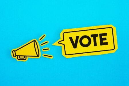 Megaphone drawing on the cut yellow paper makes “Vote” announcement. Horizontal composition with copy space. Communication Concept.