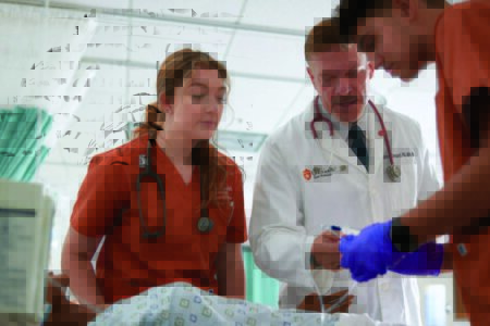 Students observe faculty member conducting medical procedure on manikin.