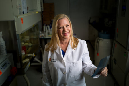 Dr. Gonzales is wearing a white coat in her lab while smiling.