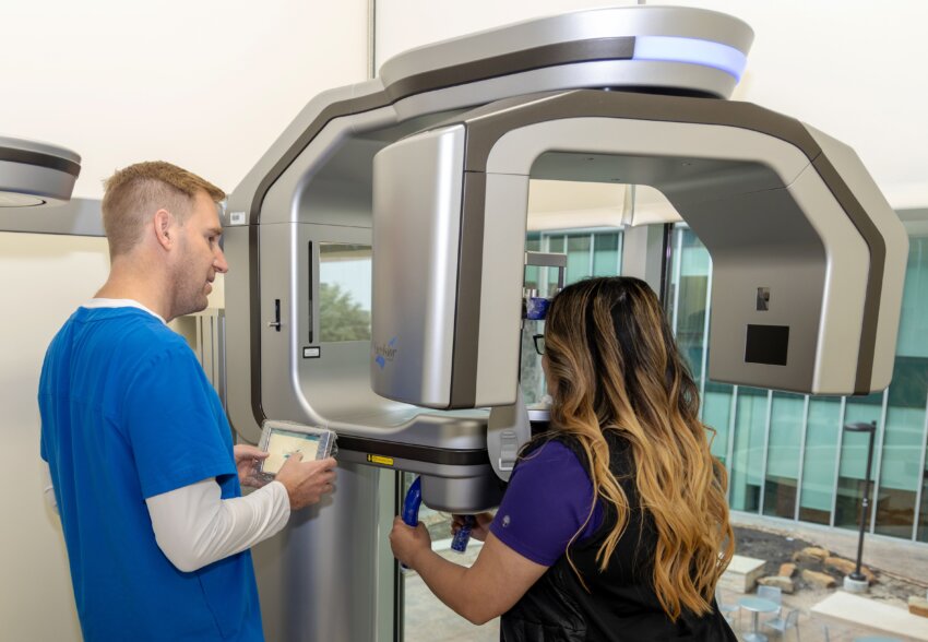 A patient stands while receiving advanced imaging and a specialist operates the equipment.