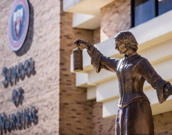 Outdoor photo of the School of Nursing's sign and its Florence Nightingale Statue.