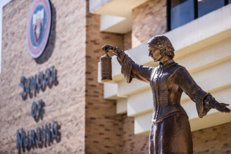 Outdoor photo of the School of Nursing's sign and its Florence Nightingale Statue.
