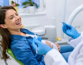 Pregnant patient smiles at dentist while in the dental chair.