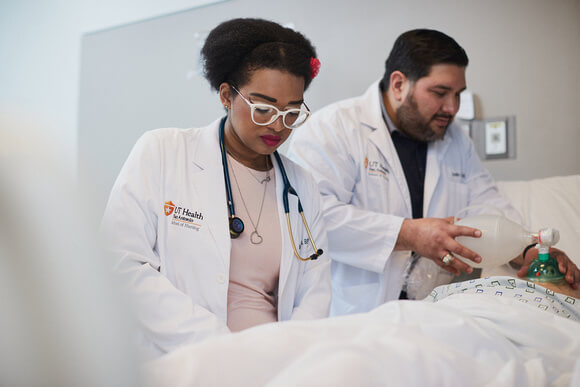 Nursing students in their white coats practice their clinical skils in class.