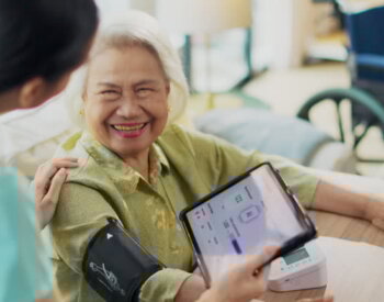 Woman asian nurse taking blood pressure of a senior woman patient at home.Home care healthcare professional using digital tablet