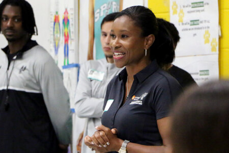 Woman stands in front of a classroom with her hands clasped in front of her chest.
