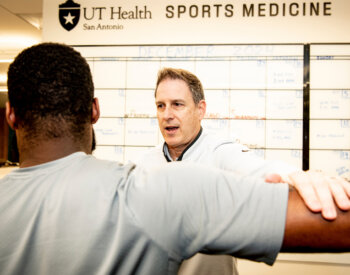 Man tests the strength of a patient's arms by pushing down on them.
