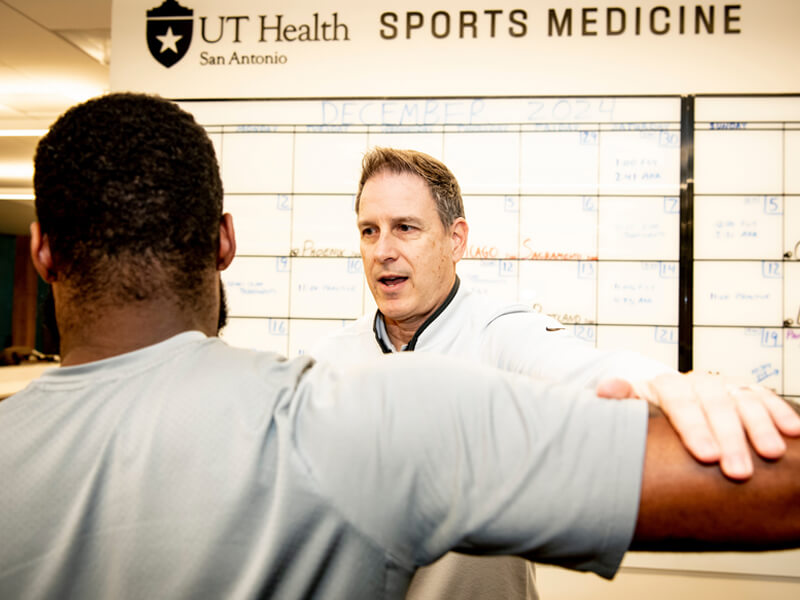 Man tests the strength of a patient's arms by pushing down on them.