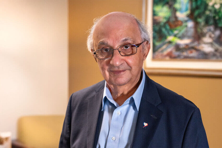 Man in suit and glasses stands in front of artwork.