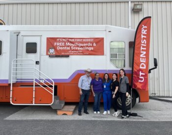 Volunteers from the School of Dentistry stand for a photo in front of the mobile dental clinic.