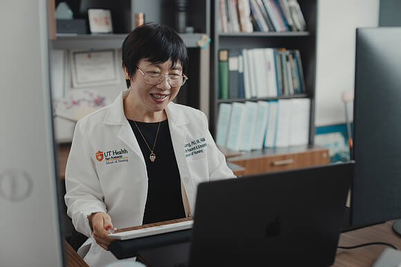 Dr. Song smiling while in a virtual meeting on her laptop.