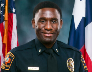 officer stands in front of Texas and U.S. flags.