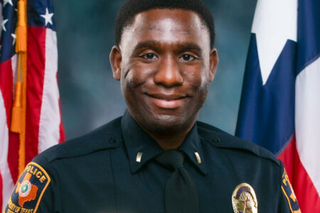 officer stands in front of Texas and U.S. flags.