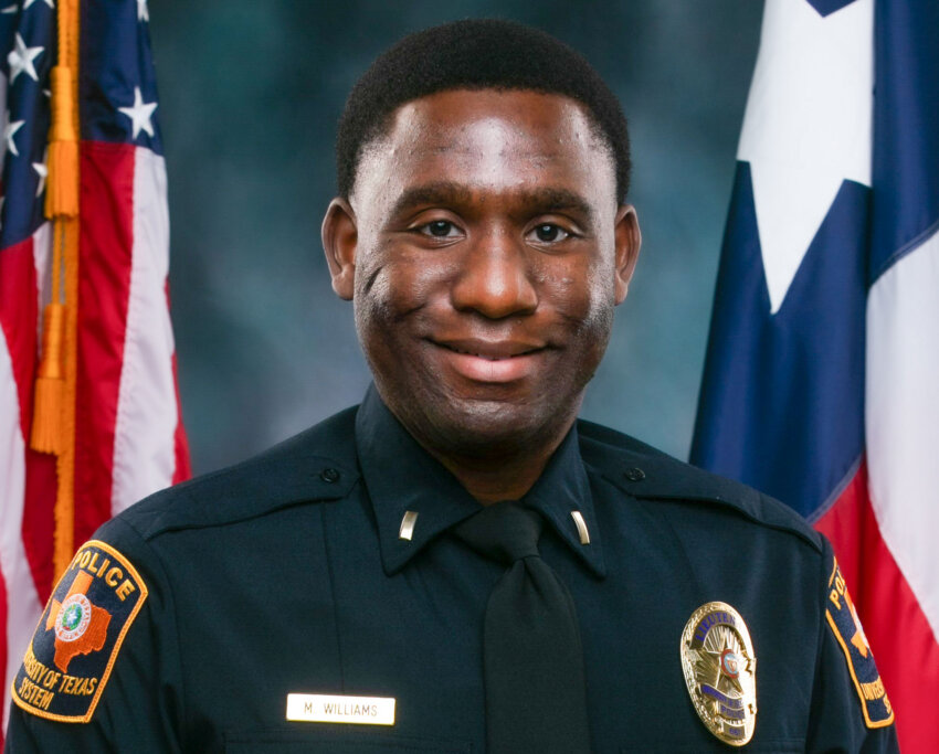 officer stands in front of Texas and U.S. flags.