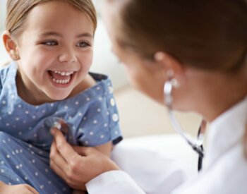 Happy child, girl and stethoscope of health provider for medical consulting, healthy lungs and listening to heartbeat. Face of laughing kid, pediatrician and chest assessment for healthcare analysis in clinic.