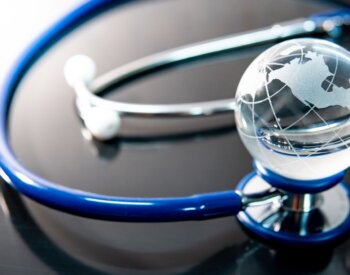 Global healthcare concept. World globe crystal glass on blue stethoscope on glossy desk. Health and medical science. Worldwide wellness business