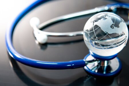 Global healthcare concept. World globe crystal glass on blue stethoscope on glossy desk. Health and medical science. Worldwide wellness business