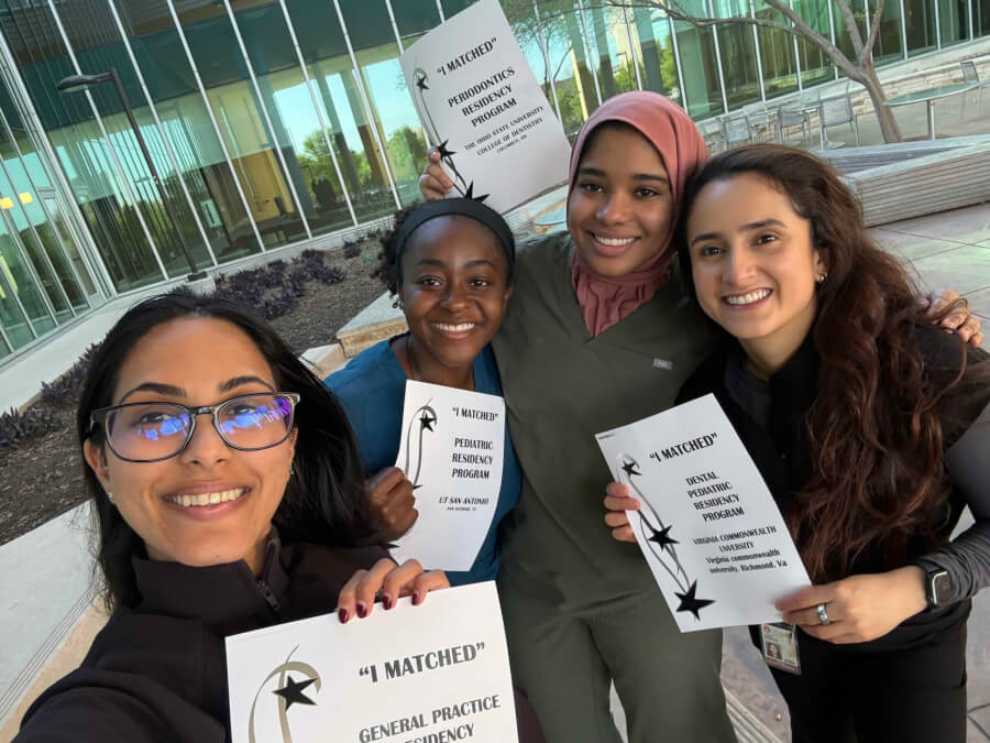 A group of dental students smile hold up signs of the program they have been matched to.