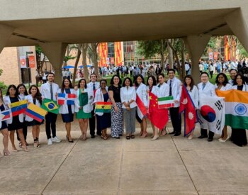 International dental students lined up in their newly-issued white coats hold their country's flag.