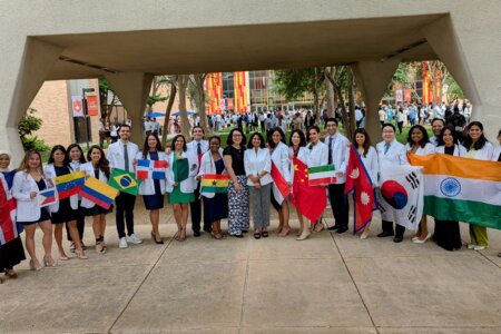 International dental students lined up in their newly-issued white coats hold their country's flag.