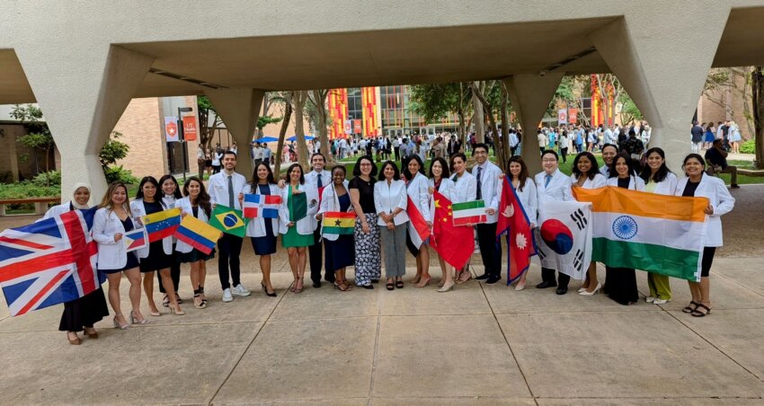 International dental students lined up in their newly-issued white coats hold their country's flag.